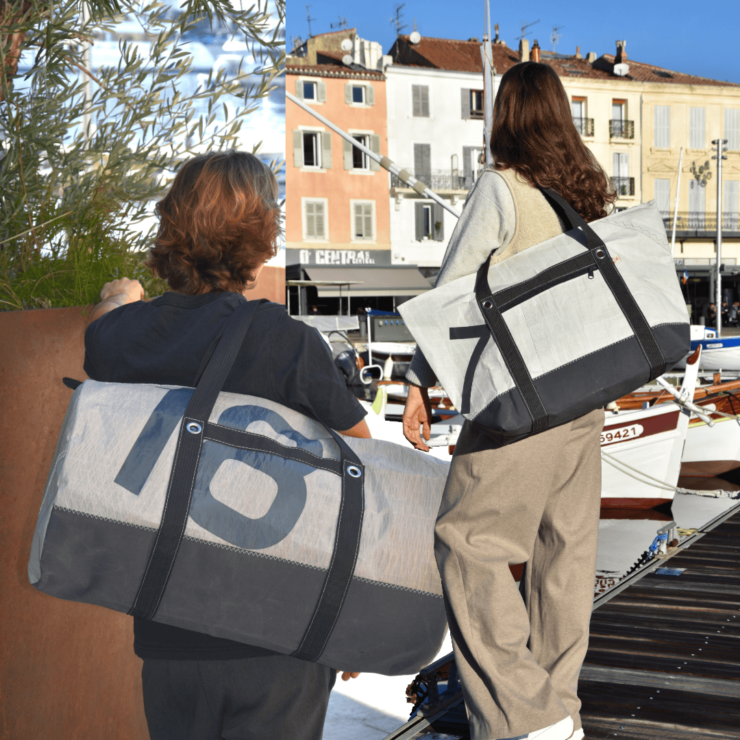 Un homme et une femme sur le Vieux-Port de La Ciotat, portant chacun un sac de voyage fabriqué en France à partir de voiles de bateau recyclée.